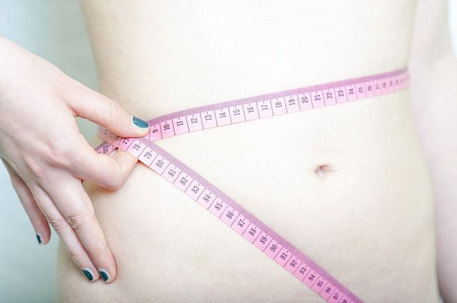 Hubená žena s nahým břichem si měří obvod krejčovským metrem